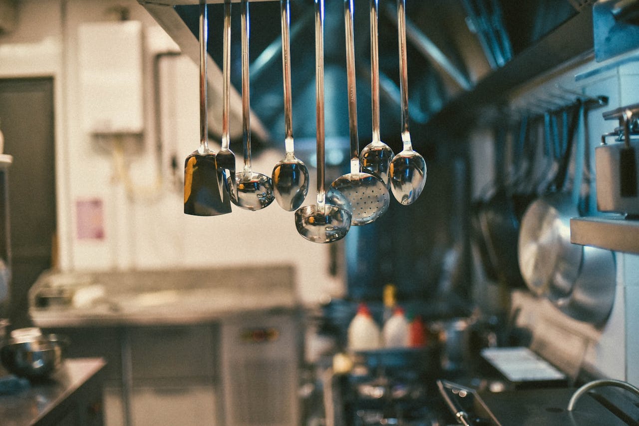 Stainless steel kitchen utensils hanging in a modern kitchen setting with blurred background.