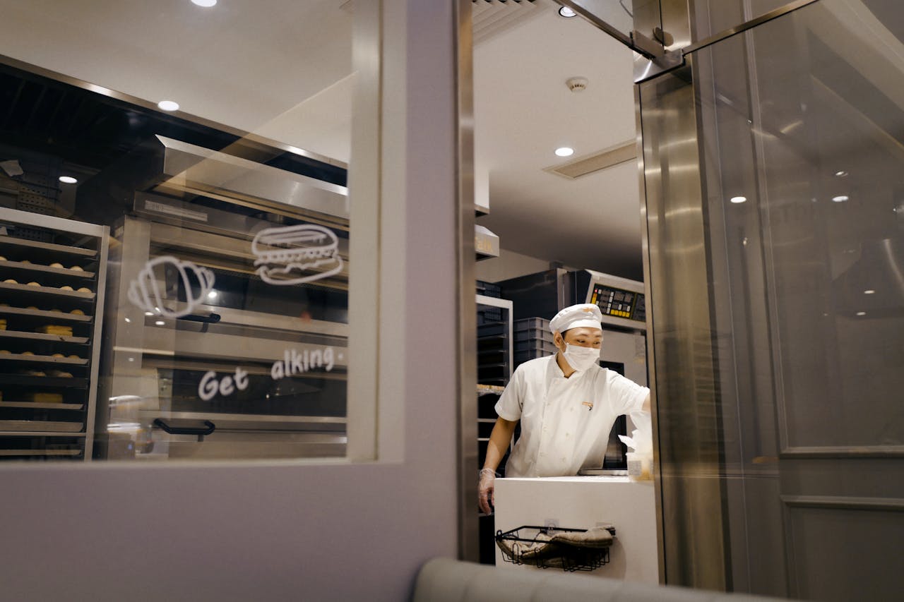Baker in a commercial kitchen preparing baked goods with professional equipment.